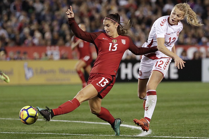 FILE - In this Jan. 21, 2018, file photo, United States forward Alex Morgan, left, shoots on goal as Denmark forward Stine Larsen, right, defends during the second half of an international friendly soccer match in San Diego. She’s already an internationally recognized soccer player with a World Cup title and an Olympic gold medal. She’s also the author of a series of kids’ books. Now you can add actor to Alex Morgan’s resume. The U.S. national team forward makes her theatrical debut in a new feature “Alex & Me” about a young player who is inspired by Morgan. (AP Photo/Gregory Bull, File)