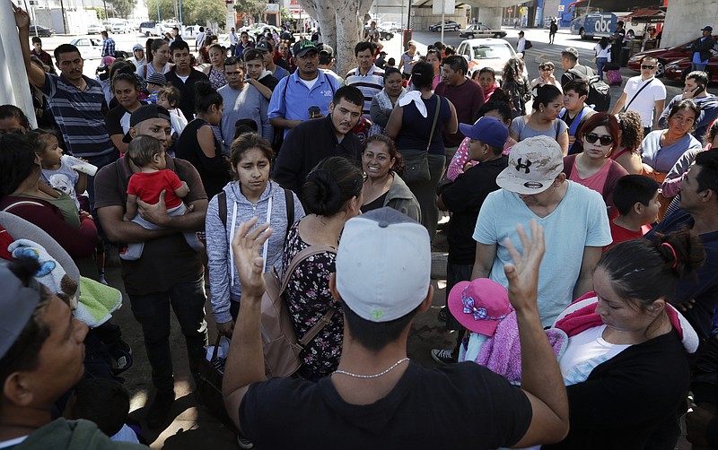 In this June 13, 2018 photo, an organizer, foreground, speaks to families as they wait to request political asylum in the United States, across the border in Tijuana, Mexico. In Tijuana, Latin Americans fleeing drug violence in their countries are camped out and waiting to apply for U.S. asylum - undeterred by the new directive from Attorney General Jeff Sessions this week to bar victims of gang violence from qualifying. (AP Photo/Gregory Bull)