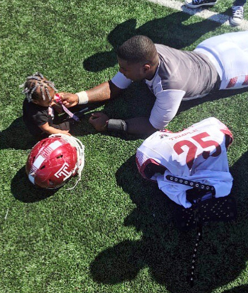 In this 2016 photo, Temple running back Ryquell Armstead plays on the field with his daughter Ry-kail during spring NCAA college football practice in Philadelphia. David Hood and  Armstead shared a position and an apartment while playing for Temple. They also shared the experience of being fathers on top of students and football players.