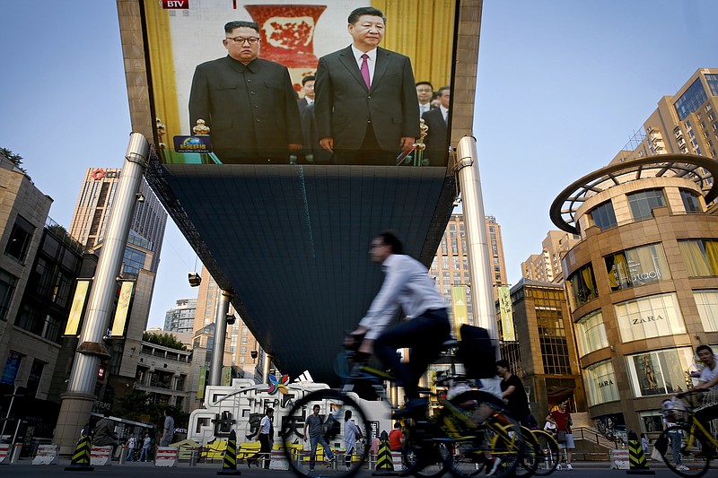 People bicycle past a giant TV screen broadcasting the meeting of North Korean leader Kim Jong Un and Chinese President Xi Jinping during a welcome ceremony at the Great Hall of the People in Beijing, Tuesday, June 19, 2018. Kim is making a two-day visit to Beijing starting Tuesday and is expected to discuss with Chinese leaders his next steps after his nuclear summit with U.S. President Donald Trump last week. (AP Photo/Andy Wong)
