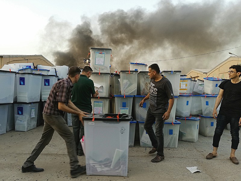 FILE - In this Sunday, June 10, 2018 file photo, Iraqi electoral officials work to salvage ballot boxes as smoke rises from a fire that broke out at Baghdad's largest ballot box storage site, where ballots from Iraq's May parliamentary elections are stored, in Baghdad, Iraq. On Thursday, June 21, 2018, Iraq's Supreme Court endorsed a manual recount of all ballots from last month's national elections, but rejected the invalidation of ballots from abroad and from voters displaced by recent conflict. (AP Photo/Karim Kadim, File)