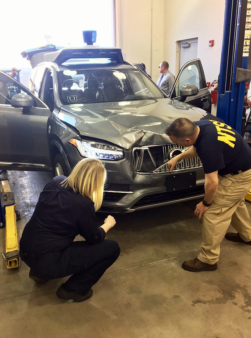 FILE - In this March 20, 2018 file photo provided by the National Transportation Safety Board, investigators examine a driverless Uber SUV that fatally struck a woman in Tempe, Ariz.  An Arizona police report says the human backup driver the Uber autonomous SUV was streaming a television show on Hulu just before the vehicle struck and killed a pedestrian in March. The Arizona Republic reported that the driver was watching “The Voice,” a television musical talent show. The newspaper received the more than 300-page report from Tempe police on Thursday, June 21.  (National Transportation Safety Board via AP)