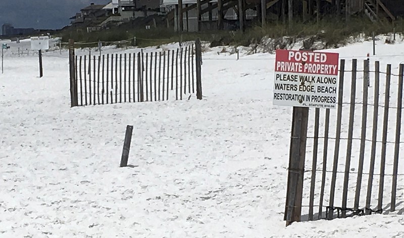 This May 15, 2018 photo shows a sign at the edge of a public beach marking where private beaches begin in Santa Rosa Beach, Fla. A new Florida law is set to reignite a fight over beach access in a Florida Panhandle county known for its pristine, sugar-white sand and rolling dunes, right in time for the July 4th holiday. Walton County Sheriff Michael Adkinson says the law that takes effect July 1 will void a local ordinance that allows public access to sand that's owned by beachfront property owners. If unwelcome beachgoers refuse to leave, they'll be arrested for trespassing. (AP Photo/Brendan Farrington)