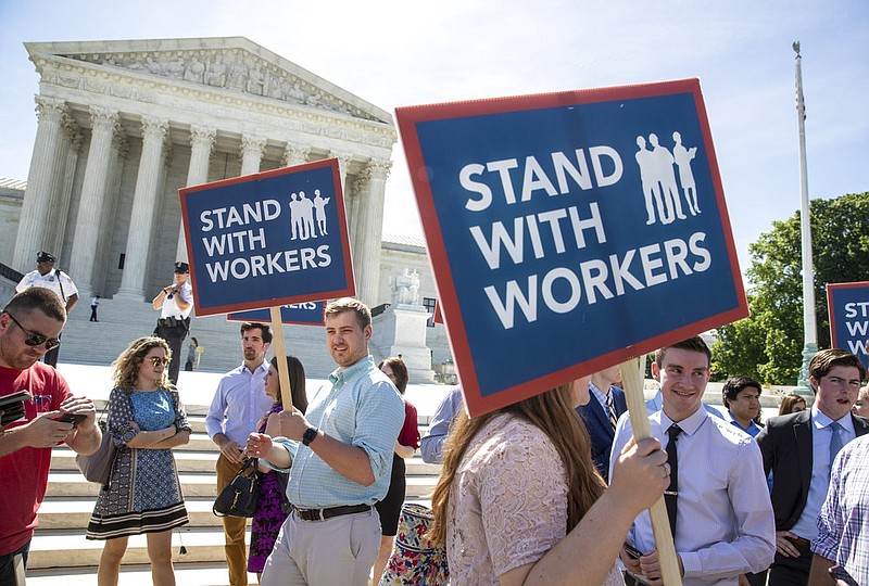 In this Monday, June 25, 2018 photo, people gather at the Supreme Court awaiting a decision in an Illinois union dues case, Janus vs. AFSCME, in Washington. The Supreme Court says government workers can't be forced to contribute to labor unions that represent them in collective bargaining, dealing a serious financial blow to organized labor.