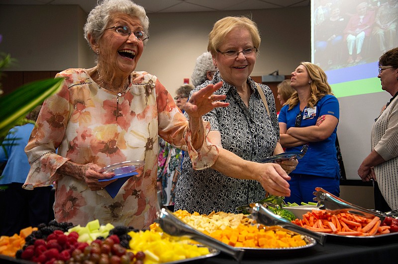 In this June 22, 2018 photo, Anna Mae Walter, left, waves to her friends during her 100th birthday party at Texas Health Presbyterian Denton in Denton, Texas. Walter's daughter Kathy Edman, right, looks on. Walter has been a volunteer at the hospital's front desk for many years but her volunteer work goes back to World War II when she was a Gray Lady for the American Red Cross, rolling bandages. (Jake King/The Denton Record-Chronicle via AP)