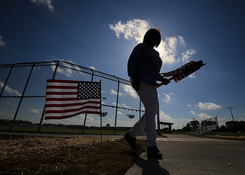 In this Wednesday, July 4, 2018 photo, Tamara Kelley puts out American flags at the new College Station Community Sports Complex in College Station, Ark., before a ribbon cutting ceremony for the complex. The town struck by a tornado 21 years ago finally has a new baseball complex in an area devastated by the storm. (Staton Breidenthal/The Arkansas Democrat-Gazette via AP)