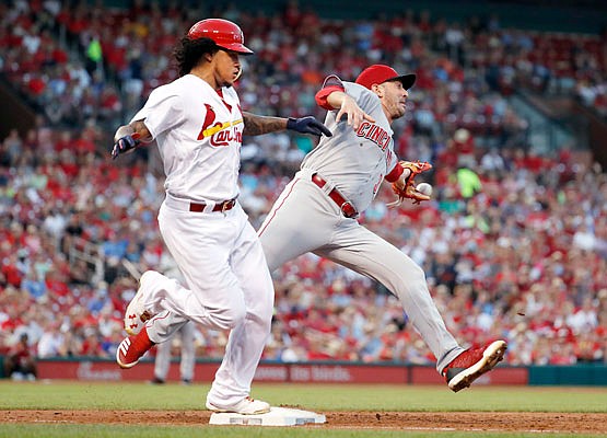 Carlos Martinez of the Cardinals is safe at first for a single as the throw gets past the glove of Reds starting pitcher Matt Harvey during the second inning of Friday night's game at Busch Stadium.