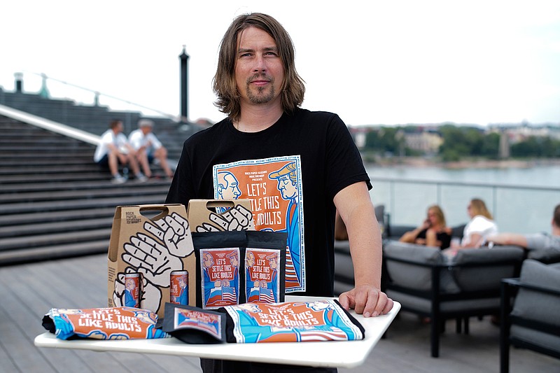 Samuli Huuhtanen, CEO of Finnish beer brewery Rock Paper Scissors poses with beer, coffee and T- shirts, labeled with cartoon caricatures depicting Russian President Vladimir Putin and U.S President Donald Trump, during an interview with the Associated Press in Helsinki, Saturday, July 14, 2018. A small Finnish craft brewery is paying a humorous tribute to the July 16 Helsinki summit by a limited-edition lager beer depicting cartoon U.S. and Russian presidents on its label with a text urging Donald Trump and Vladimir Putin to settle things "like adults".   (AP Photo/Markus Schreiber)