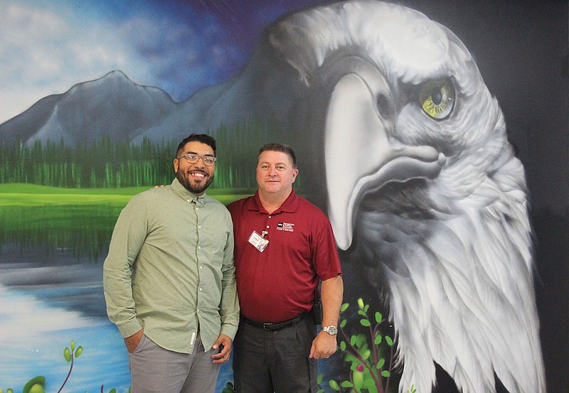 Anthony Rose, left, stands with Warden Michael Upshaw on July 20 in front of a mural Rose created during his incarceration at Cleveland Correctional Center in Cleveland, Texas. Upshaw pushed Rose to engage in creativity as Rose started to go through the prison's business entrepreneurship program. Upshaw's challenge involved creating some murals around the prison.