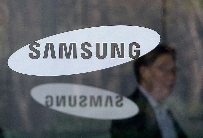 FILE - In this April 6, 2018, file photo, an employee walks past logos of the Samsung Electronics Co. at its office in Seoul, South Korea. Samsung Electronics says it will spend $22 billion over the next three years on artificial intelligence, auto components, and other future businesses. (AP Photo/Ahn Young-joon, File)