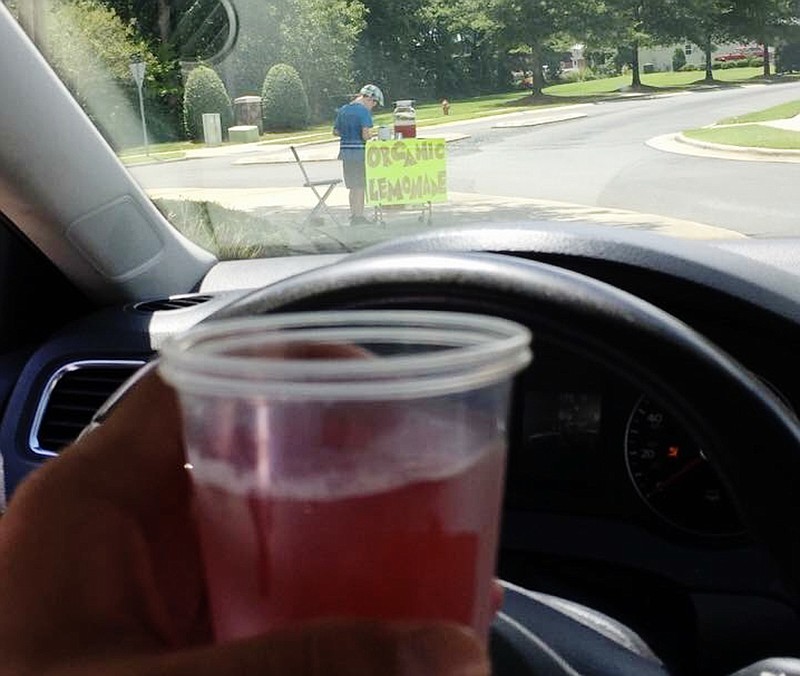 This Aug. 4 2018, photo provided by James Castellano, of Monroe, N.C., shows a drink he bought from a boy, background, in Monroe. Deputies in North Carolina have arrested a suspect who they say robbed the 9-year-old lemonade vendor of $17 at gunpoint, an incident which led to more than $200 in donations and a riding lawn mower, Tony Underwood of the Union County Sheriff's Office said Wednesday. (James Castellano via AP)