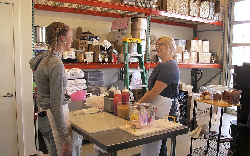 In this photo taken June 8, 2018, craft donut shop owner Amy Pruchnic, right, talks with an employee at her busy new store in downtown Spokane, Wash. The state's second-largest city is booming these days thanks to a good economy and influx of new residents. (AP Photo/Nicholas K. Geranios)