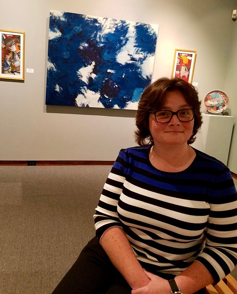 Dr. Becky Black, the new visual arts and community programs coordinator for the Texarkana Regional Arts and Humanities Council, sits in the secure gallery at the Regional Arts Center. The blue, black and white abstract artwork behind her is one of her favorites from the 30th annual Juried Exhibition.

