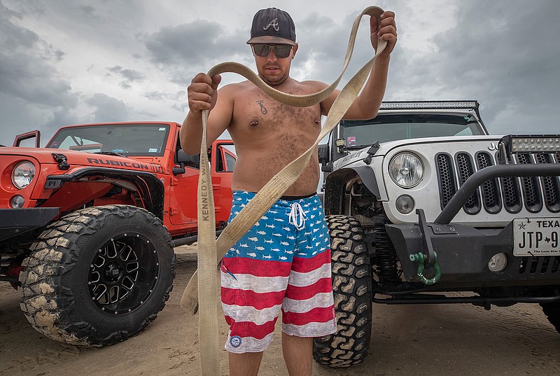 Justin "Gator" Glatthaar, a member of Bolivar Beach Vehicle Rescue, unfurls his tow rope during a gathering with other group members at Crystal Beach on the Bolivar Peninsula on Saturday, Aug. 4, 2018. The group of truck and SUV drivers provide free tow outs to beachgoers stuck in sand on Bolivar beaches. (Stuart Villanueva/The Galveston County Daily News via AP)