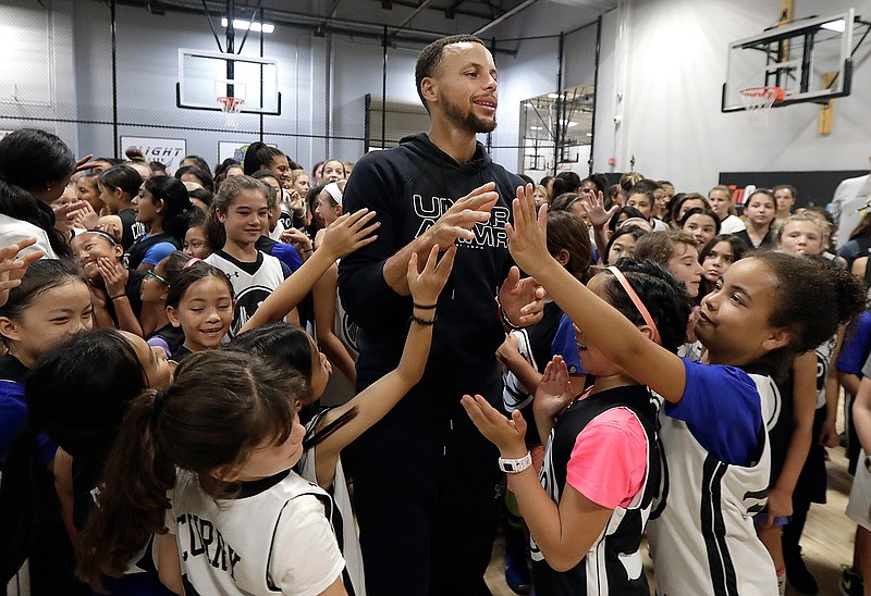 Golden State Warriors' Stephen Curry, center, greets basketball camp participants after taking a group photo at Ultimate Fieldhouse in Walnut Creek, Calif., Tuesday, Aug. 14, 2018. For the first time, Curry hosted only girls for a free, Warriors-run camp Monday and Tuesday at Walnut Creek's Ultimate Fieldhouse. Last week at the same facility that he has also chosen in recent years, the Golden State star held his Under Armour "Stephen Curry Select Camp" with two of the nation's top high school girls playing mixed right in with the best boys. The two-time MVP and father of two young daughters has made it his mission to better support the girls' game. He asked longtime Warriors camp director Jeff Addiego to plan an all-girls session this summer. (AP Photo/Jeff Chiu)