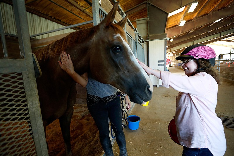 In a Tuesday, Aug. 21, 2018 photo, Lauren Hall gives Ernie the horse a treat at SIRE Houston Therapeutic Horsemanship, in Richmond, Texas. This horseback riding facility in Richmond helps all. Some people go to the facility to heal from a physical injury, and others come to cope with other health issues. Nearly a year after a Ernie came to SIRE Houston Therapeutic Horsemanship barely hanging on after Hurricane Harvey ravaged homes and buildings in Houston, he is now fully recovered.   (Karen Warren/Houston Chronicle via AP)