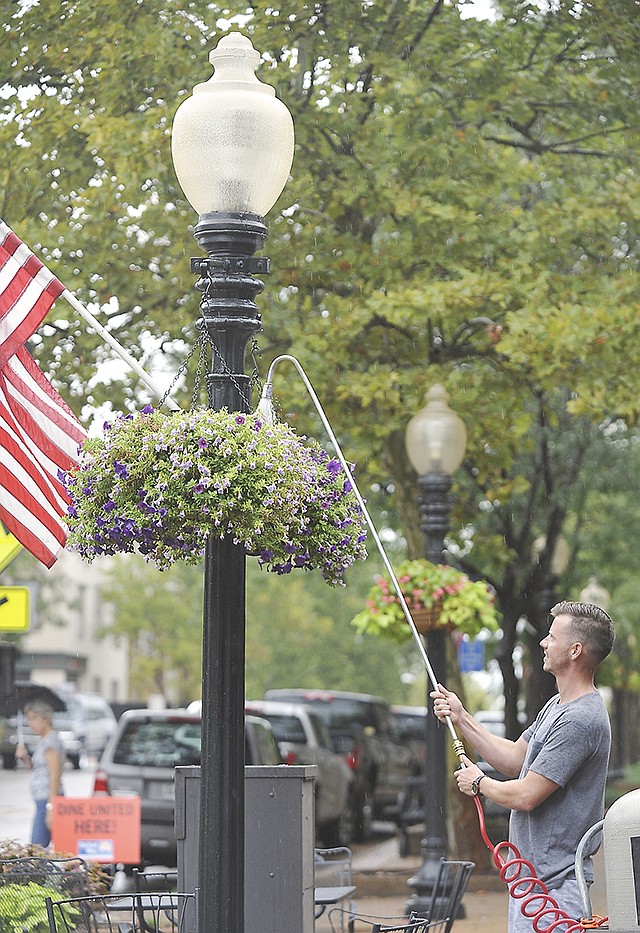 Tyler Young of River City Florist waters the downtown hanging plant baskets Friday amid the afternoon sprinkle of rain.