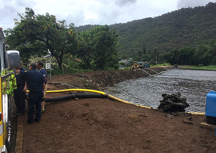 Officials pump water from a reservoir where a dam came close to overflowing in Honolulu on Thursday, Sept. 13, 2018. Honolulu officials say they may need to evacuate 10,000 people from a residential neighborhood if water in the reservoir continues to rise after heavy rains from a tropical storm. (AP Photo/Caleb Jones)