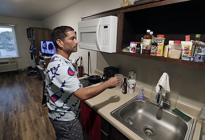 In this Monday, Sept. 10, 2018, photo, Jose Santiago checks on items in the kitchenette in his room at the WoodSpring Suites in Orlando, Fla. Santiago, like many Puerto Rican evacuees, has until Friday to find a place to live. (AP Photo/John Raoux)