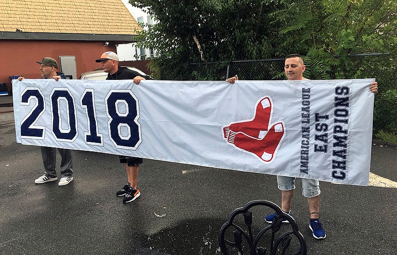 In this Tuesday, Sept. 18, 2018 photo, friends hold a banner they found in Somerville, Mass., that proclaims the Boston Red Sox are the 2018 American League East Champions, though the team has not yet clinch the division. A Red Sox spokesman said the banner apparently fell off a vendor's delivery truck, and planned to send a courier to retrieve the banner Wednesday. (Ted Daniel/Boston 25 News via AP)