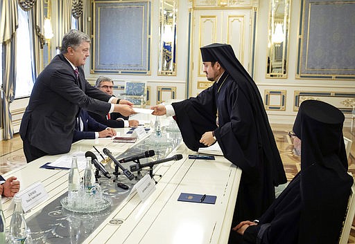 Archbishop Ilarion of Edmonton from Canada, center, hands over a message from Ecumenical Patriarch Bartholomew to Ukrainian President Petro Poroshenko while Archbishop Daniel of Pamphilon from the United States, right, watches during their meeting in Kiev, Ukraine, Monday, Sept. 17, 2018. The Ecumenical Patriarchate has appointed two exarchs in Kiev for the framework of the preparations for the granting of autocephaly to the Orthodox Church in Ukraine. (Mikhail Palinchak/Presidential Press Service Pool Photo via AP)