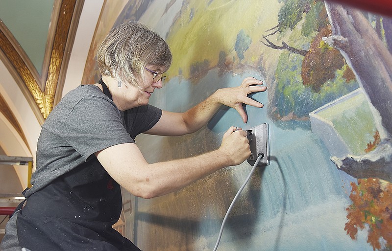 Wendy Partridge applies heat to the lunette painting "Power from the Hills" in an effort to promote the job of the adhesive that has been brushed on the work. The painting on canvas that is adhesed to the wall is located in the northwest corner of the second floor mezzanine in the Capitol. Partridge is one of two working for ICA-Art Conservation of Cleveland, Ohio.