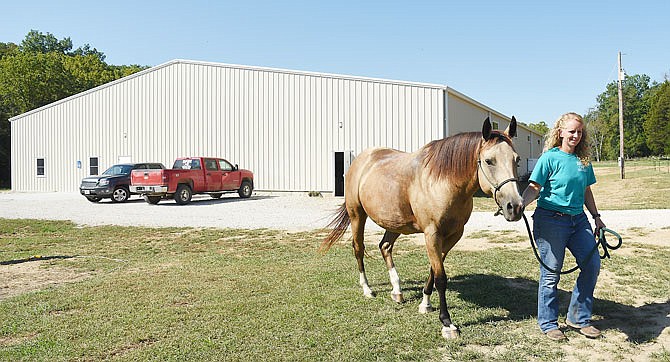 Amy DeCramer, executive director of Healing Horses Therapeutic Riding in Linn, leads Dixie, an 8-year-old buckskin quarter horse, back to the pasture after working with her at the indoor arena, seen in background. The protected riding area is a relatively new addition that provides opportunities to be able to ride in a protected environment. 