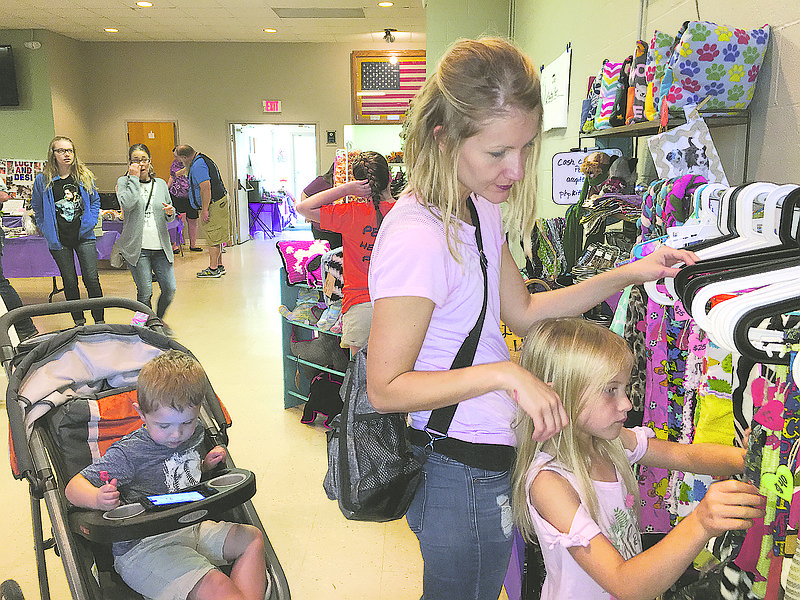 Jessica Voss and daughter Chloe, 6, look over clothes at the Stitched By Heart booth at Sunday's annual Caring for Critters fundraiser. The event was sponsored by People Helping Paws. Meanwhile, Voss' 3-year-old son, Gage, is occupied with a portable electronic device. Money raised at the Sunday event, held at American Legion Post 5, will help with People Helping Paws animal rescue/adoption efforts.