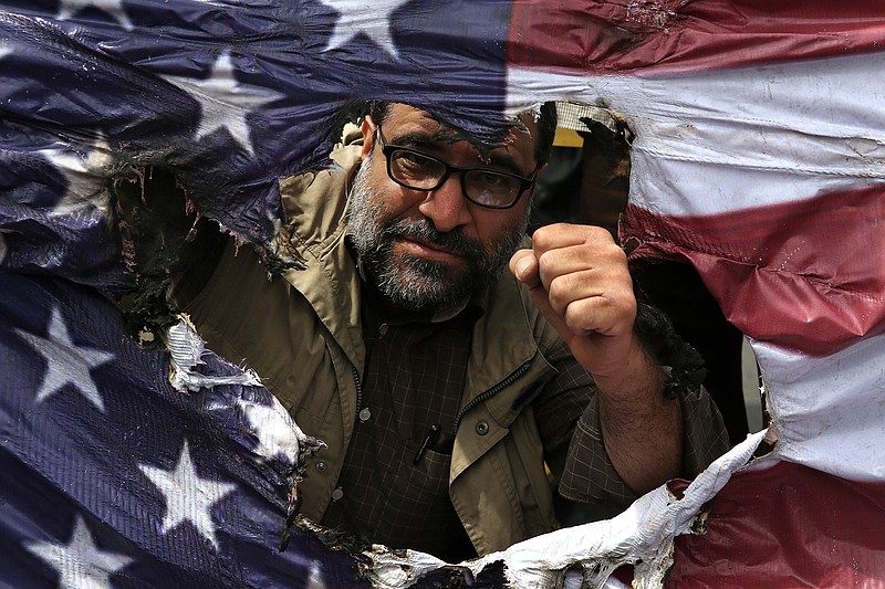 An Iranian protestor clenches his fist behind a burnt representation of the U.S. flag May 11 in Tehran, Iran, during a protest over U.S. President Donald Trump's decision to pull out of the nuclear deal with world powers. Ahead of the 40th anniversary of Iran's Islamic Revolution, the country's government is allowing more criticism to bubble up to the surface. But limits still clearly exist in Iran's Shiite theocracy.