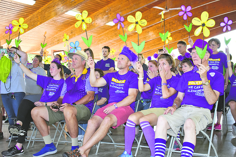 Participants in Sunday's 2018 Walk to End Alzheimer's for Jefferson City hold up their flowers before the walk at Ellis-Porter Riverside Park. The yellow flowers are held by those caring for someone with Alzheimer's and the purple are by those who lost someone to the disease. Blue flowers were for people who have the disease, and orange flowers were by people who don't have a direct connection to the disease. 