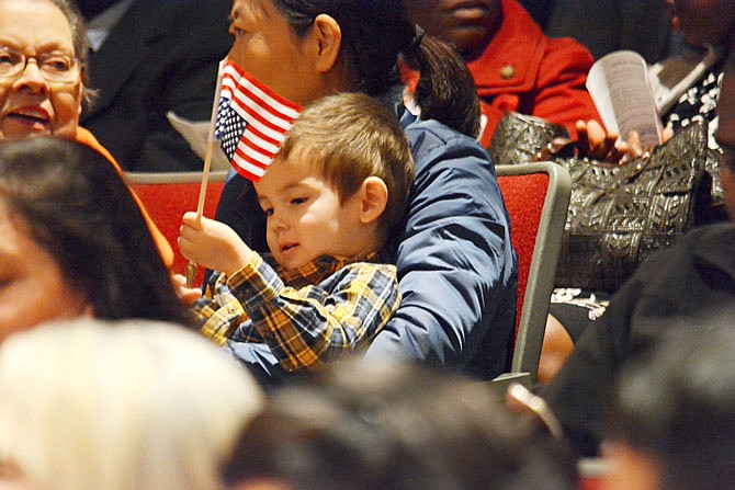 Thomas Ritts, 3, plays with an American flag Friday during a Naturalization Ceremony at the Missouri National Guard. Thomas attended with his mother, Wen Ritts, background, as she became a citizen. 