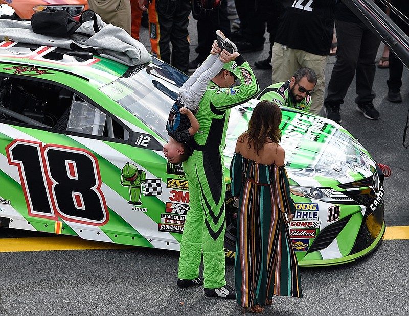 Kyle Busch, center, holds his son Brexton by the legs before a NASCAR Cup Series auto race, Sunday, Oct. 7, 2018, at Dover International Speedway in Dover, Del. Busch's wife Samantha, right, looks on. (AP Photo/Nick Wass)