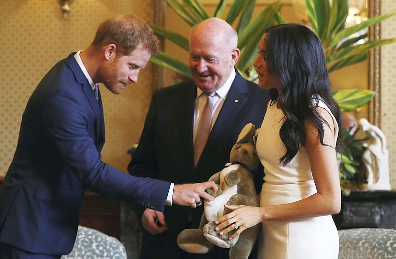 Britain's Prince Harry, right, reacts as Meghan, right, Duchess of Sussex holds a toy kangaroo given by Australia's Governor General Sir Peter Cosgrove, center, in Sydney, Australia, Tuesday, Oct. 16, 2018. (Phil Noble/Pool Photo via AP)