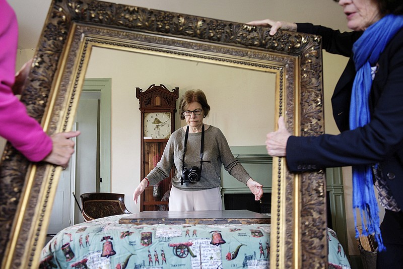 In this Monday, Sept. 24, 2018 photo, Art appraiser Mary Jane Clark, of Wilder, Vt., looks over a painting of 19th-century American lawyer and politician Daniel Webster as Hanover Historical Society Treasurer Betsy Gonnerman, left, and President Cyndy Bittinger carry away its frame at the Webster Cottage in Hanover, N.H. A frightening moment when the painting dropped onto a quilt as its frame was lifted turned productive when Clark was able to more closely examine the edges of the canvas. "This happens a lot with old frames and old work," said Clark. "Paintings come out." ( James M. Patterson /The Valley News via AP)