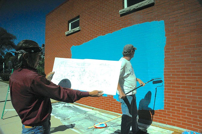 Muralist Dennis Holliday considers a sketch for a 60-by-10-foot mural, highlighting scenes at the Moniteau County Fair, while Danny Bentzen paints a base coat on the Moniteau County Historical Society's genealogy library wall facing South Street.