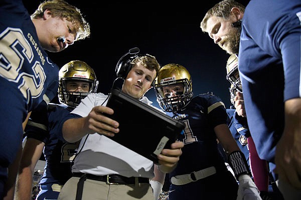 Helias assistant coaches Conner White (center) and Jeff Pickering and shows players video of a play on the sideline during last Friday night's game against De Smet at Ray Hentges Stadium.