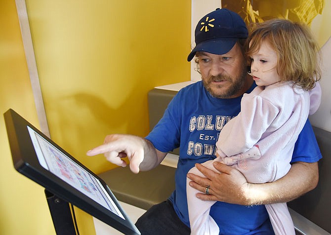 Douglas Goertz shows his 2-year-old daughter, Violet Goertz, how to view library checkouts Tuesday on an electronic tablet. The pair visited the digital bookmobile that was parked in front of Missouri River Regional Library. Goertz said his wife and daughter visit the library on occasion to avail themselves of computers and printers, along with children's programming. 