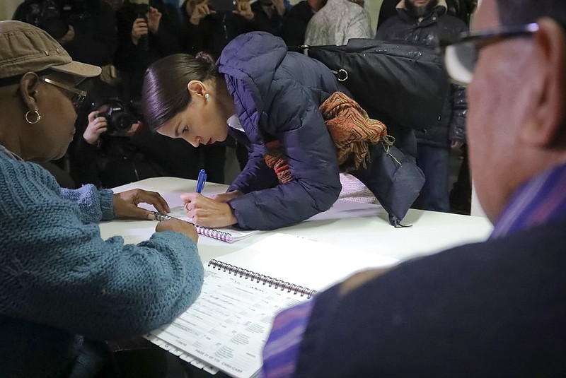 New York Democratic congressional candidate Alexandria Ocasio-Cortez, center, signs a register before voting, Tuesday Nov. 6, 2018, in the Parkchester community in the Bronx, N.Y. (AP Photo/Bebeto Matthews)