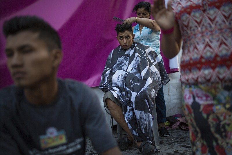 Honduran migrant Luis Fernando Barahona looks at an ongoing catholic mass while a hairdresser cuts his hair at a shelter at the Jesus Martinez stadium, in Mexico City, Wednesday, Nov. 7, 2018. Humanitarian aid converged around the stadium in Mexico City where thousands of Central American migrants winding their way toward the United States were resting Tuesday after an arduous trek that has taken them through three countries in three weeks. (AP Photo/Rodrigo Abd)