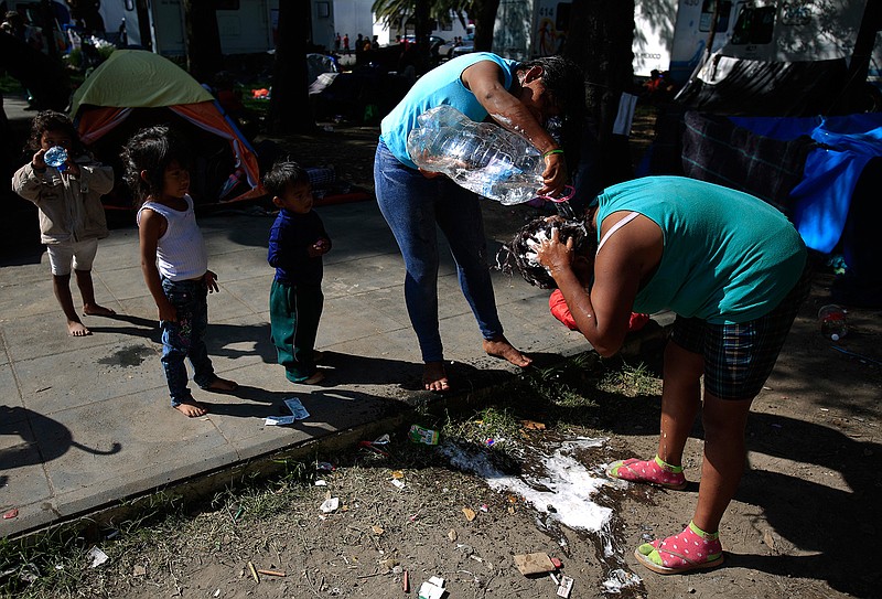 Women use water from a bottle to wash their hair in a sports complex where thousands of migrants have been camped out for several days in Mexico City, Friday, Nov. 9, 2018. About 500 Central American migrants headed out of Mexico City on Friday to embark on the longest and most dangerous leg of their journey to the U.S. border, while thousands more were waiting one day more at a massive improvised shelter.(AP Photo/Rebecca Blackwell)