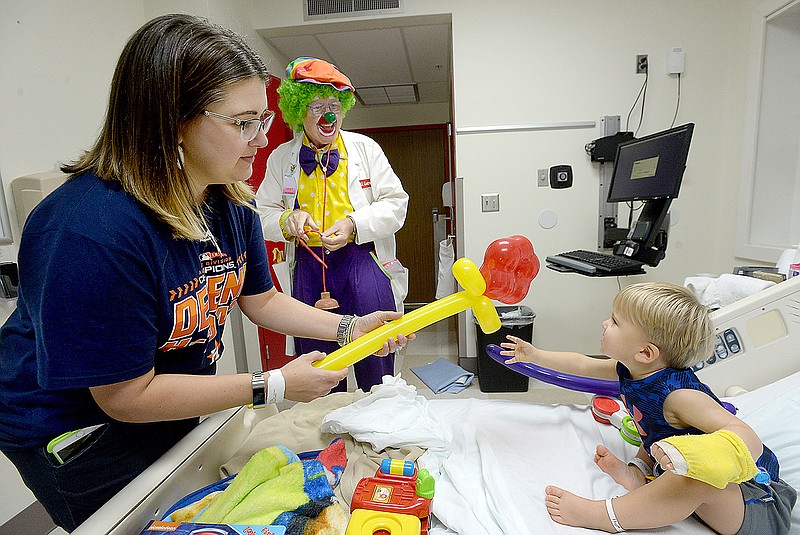 In this Friday, Oct. 5, 2018 photo, Larry Thompson, aka Dr. U. Getwell, visits with Daina Whittington and her son Cade, 2, as he makes his weekly rounds to patients and staff at Baptist Hospital in Beaumont, Texas. Thompson has been volunteering at the hospital since 2007, and calls his clown work a ministry, bringing a moment of joy to patients and families in what is often a difficult time.  (Kim Brent/The Beaumont Enterprise via AP)