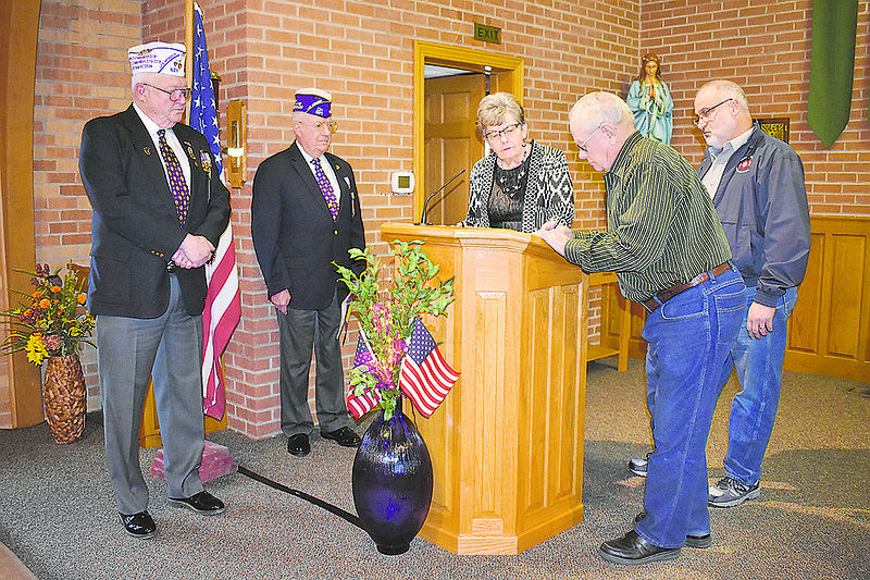 At left, John Dismer and Bryce Lockwood from the Military Order of the Purple Heart look on as Craig Koetting and Kenneth Brown sign papers for Osage Bend to be designated as a Purple Heart Village during a Sunday ceremony at St. Margaret's Catholic Church. In the middle is Rosie Verslues, who started the process for the designation.