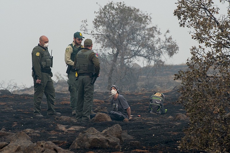 In this Thursday, Nov. 15, 2018, photo, Charlie Miles peers up at state forestry officers and state parks rangers after being arrested for trying to go home on a desolate stretch of Skyway Road between Paradise and a Chico church he was sleeping at in Paradise, Calif. (Renee C. Byer/The Sacramento Bee via AP)