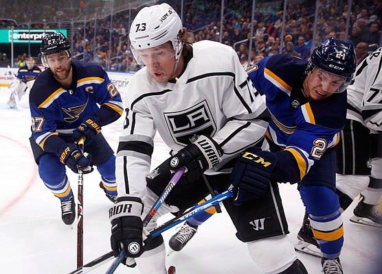 Tyler Toffoli of the Kings reaches for a loose puck along the boards between Blues teammates Alex Pietrangelo (left) and Tyler Bozak during the first period of Monday night's game in St. Louis.