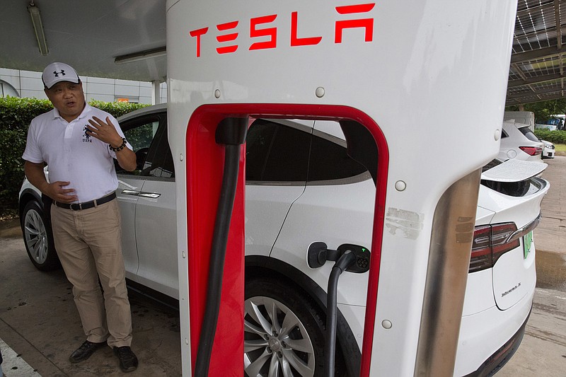 In this June 22, 2018, photo, Shan Junhua chats about privacy near his white Tesla while charging it in Shanghai. When Shan bought his white Tesla Model X, he knew it was a fast, beautiful car. What he didn't know is that Tesla constantly sends information about the precise location of his car to the Chinese government. Automakers selling electric vehicles in China send a constant feed of information about the location of cars to the government, potentially adding to the rich kit of surveillance tools available to the regime as President Xi Jinping steps up the use of technology to track Chinese citizens. (AP Photo/Ng Han Guan)