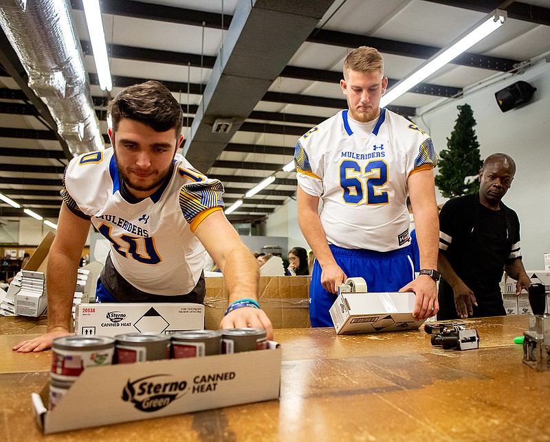 Muleriders quarterback Hayden Mallory reaches for a package of Canned Heat for left tackle Mason Harding to box Friday at the Texarkana Resources for the Disabled in Texarkana, Ark. See related story on Page 1B.