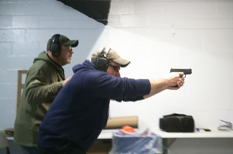 In this photo taken from a video shot on Nov. 28, 2018, Mike Carnevale places his hand on the back of Mark Hennesey while instructing him at the American Tactical Systems' indoor range in Green Island, New York. The application process for handgun licenses would be expanded under a bill before the New York state Legislature. The bill would require handgun applicants to turn over log-in information so investigators could look at three years' worth of Facebook, Snapchat, Twitter and Instagram postings. Google, Yahoo and Bing searches over the previous year also would be checked. (AP Photo/Michael Hill)