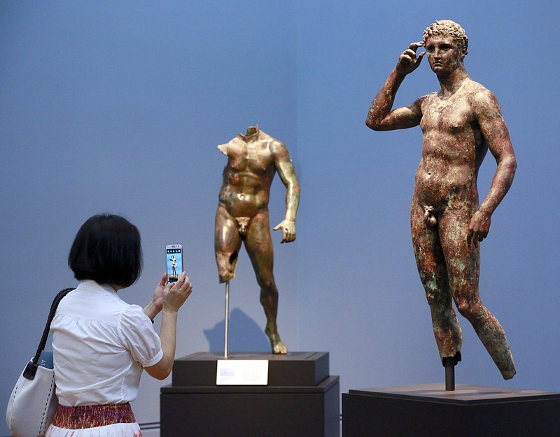 In this Monday, July 27, 2015 photo, reporter Sookee Chung takes a photo of a sculpture titled "Statue of a Victorious Youth, 300-100 B.C." at the J. Paul Getty Museum in Los Angeles. The J. Paul Getty Museum in Los Angeles has vowed to assert its right to keep an important Greek statue after Italy's highest court rejected its appeal of a ruling ordering the artwork to be returned to Italy. The ANSA news agency said Tuesday that the Court of Cassation rejected the appeal outright earlier this week. "Victorious Youth," a nearly life-sized bronze dating from 300 B.C. to 100 B.C., is one of the highlights of the Getty collection. (AP Photo/Nick Ut, File )