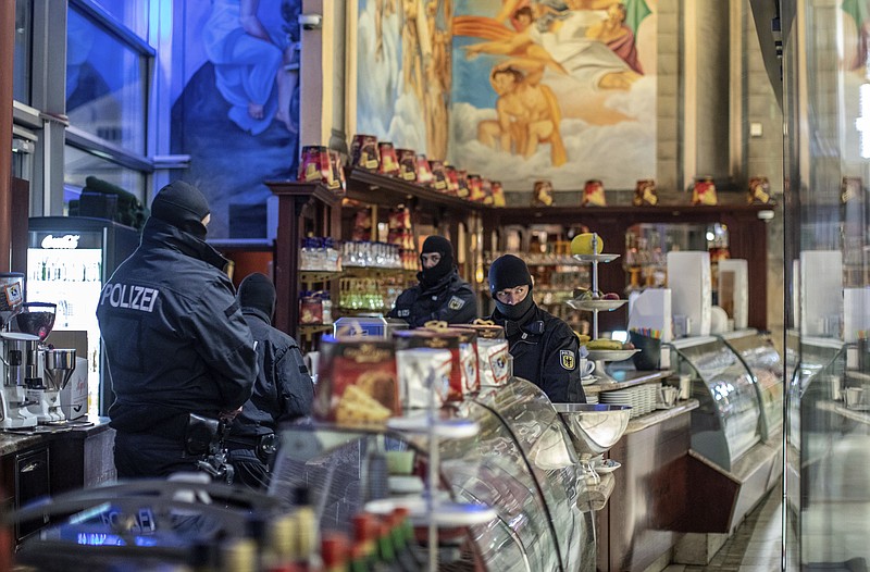 Masked police stand in an ice parlor in Duisburg, western Germany, Wednesday, Dec. 5, 2018 as authorities conduct coordinated raids in Germany, Italy, Belgium and the Netherlands in a crackdown on the Italian mafia. (Christoph Reichwein/dpa via AP)