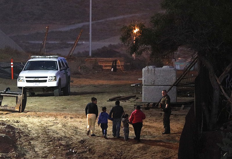 Migrants traveling with children walk up a hill to a waiting U.S. Border Patrol agent just inside San Ysidro, Calif., after climbing over the border wall from Playas de Tijuana, Mexico, Monday, Dec. 3, 2018. Thousands of Central American migrants who traveled with recent caravans want to seek asylum in the United States but face a decision between crossing illegally or waiting months, because the U.S. government only processes a limited number of those cases a day at the San Ysidro border crossing. (AP Photo/Rebecca Blackwell)